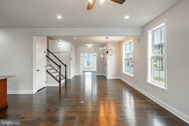 unfurnished living room featuring a wealth of natural light, dark hardwood / wood-style flooring, and ceiling fan with notable chandelier