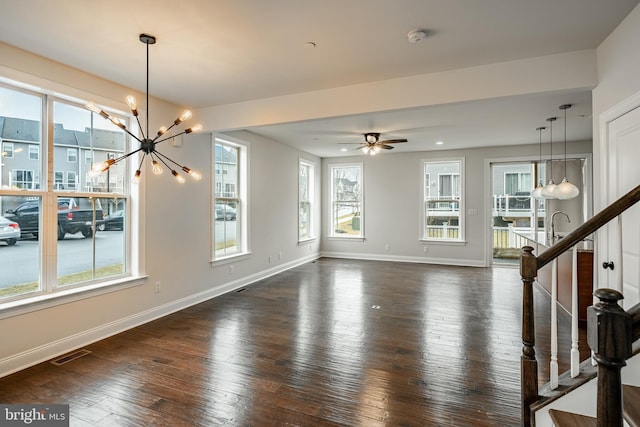 unfurnished living room featuring dark wood-type flooring, a healthy amount of sunlight, and ceiling fan with notable chandelier