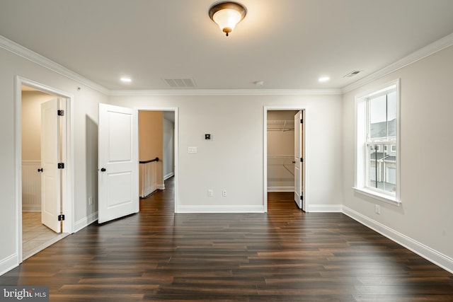 unfurnished bedroom with a closet, a spacious closet, crown molding, and dark wood-type flooring