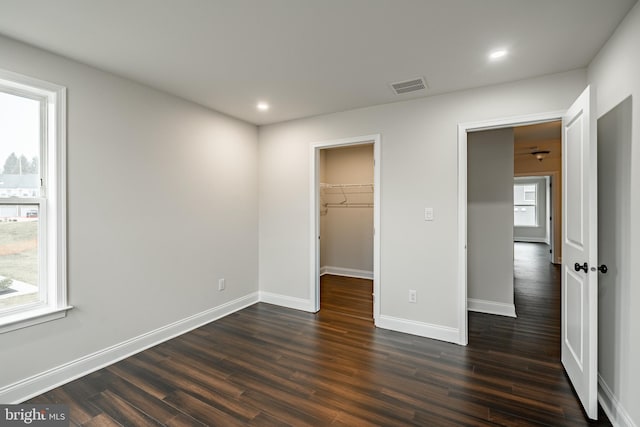 unfurnished bedroom with a closet, dark hardwood / wood-style flooring, a walk in closet, and multiple windows