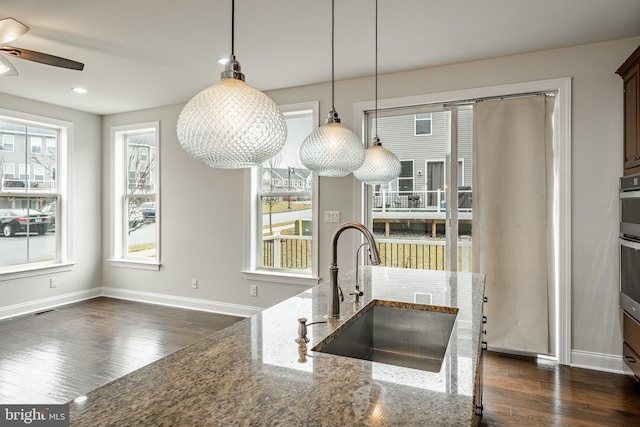 kitchen with pendant lighting, oven, sink, dark hardwood / wood-style floors, and light stone countertops