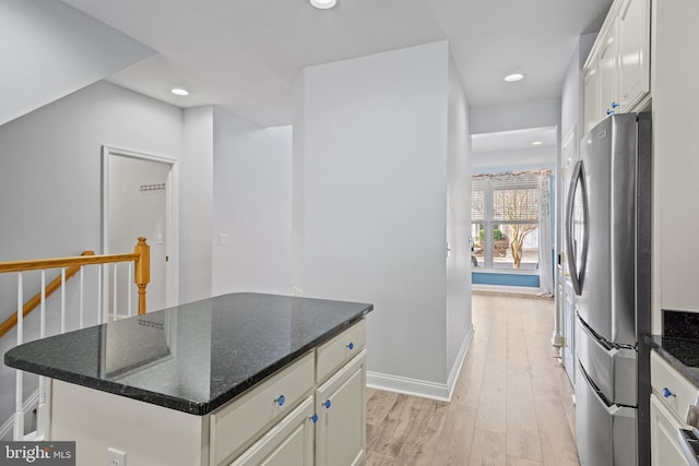 kitchen with a kitchen island, dark stone countertops, light hardwood / wood-style floors, white cabinetry, and stainless steel refrigerator