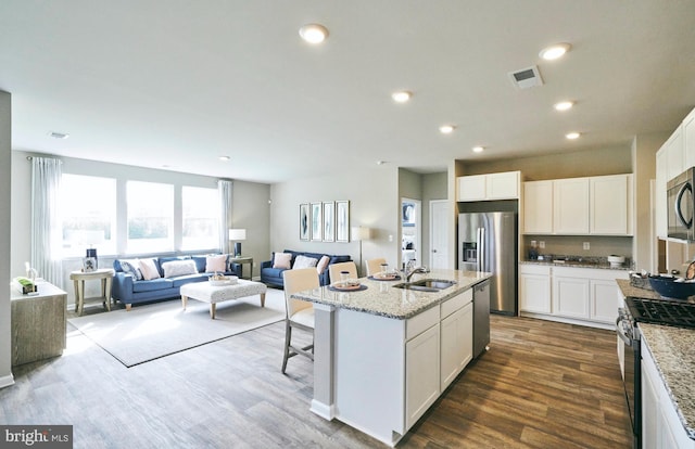 kitchen with white cabinets, stainless steel appliances, dark hardwood / wood-style floors, and a kitchen island with sink