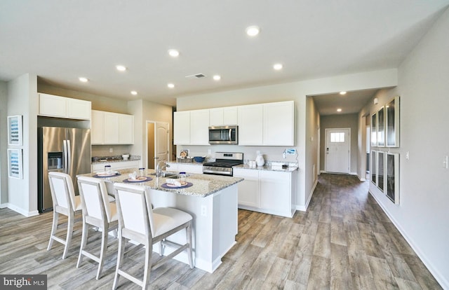 kitchen featuring white cabinetry, light stone countertops, a center island with sink, and stainless steel appliances