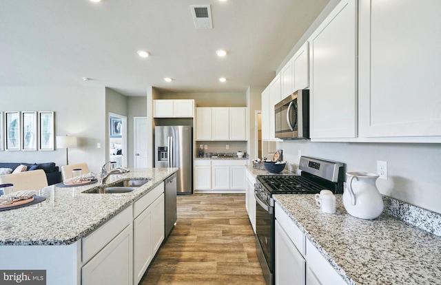 kitchen with appliances with stainless steel finishes, light wood-type flooring, a kitchen island with sink, sink, and white cabinetry