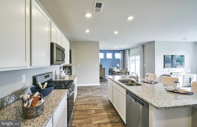 kitchen featuring appliances with stainless steel finishes, sink, white cabinets, dark hardwood / wood-style floors, and an island with sink