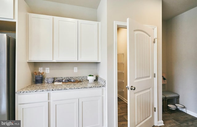 bar with stainless steel fridge, white cabinets, dark wood-type flooring, and light stone counters