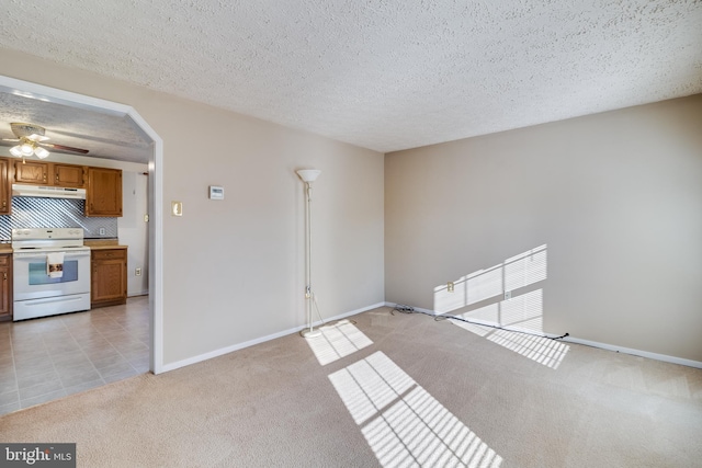 unfurnished living room featuring ceiling fan, light colored carpet, and a textured ceiling