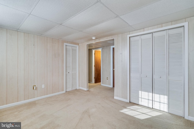 unfurnished bedroom featuring a paneled ceiling, multiple closets, wooden walls, and light colored carpet