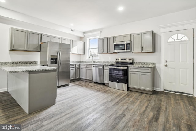 kitchen featuring dark wood-type flooring, sink, light stone countertops, appliances with stainless steel finishes, and kitchen peninsula