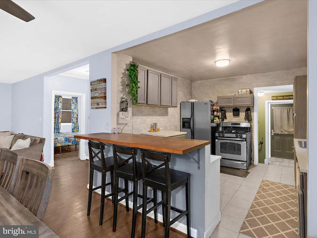 kitchen featuring stainless steel appliances, a kitchen breakfast bar, wooden counters, decorative backsplash, and light wood-type flooring