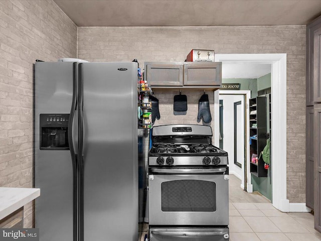 kitchen with light tile patterned flooring, stainless steel appliances, and brick wall