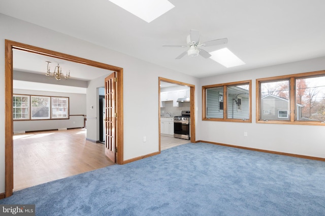 carpeted spare room featuring ceiling fan with notable chandelier and a skylight