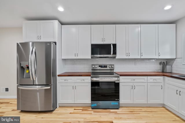 kitchen with appliances with stainless steel finishes, white cabinetry, and butcher block counters