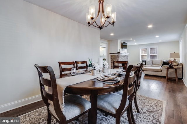 dining space with a stone fireplace, dark hardwood / wood-style floors, and an inviting chandelier