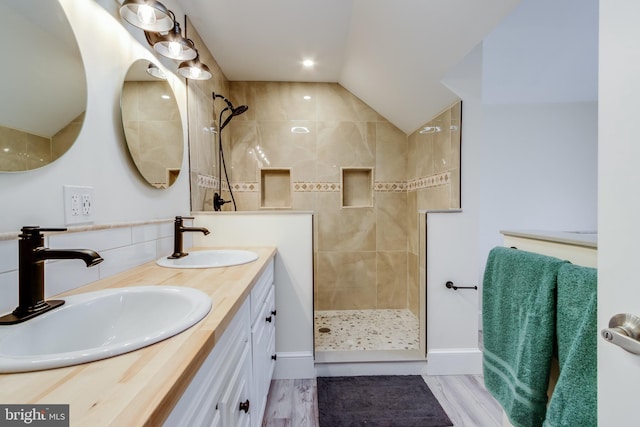 bathroom with a tile shower, vanity, vaulted ceiling, and wood-type flooring