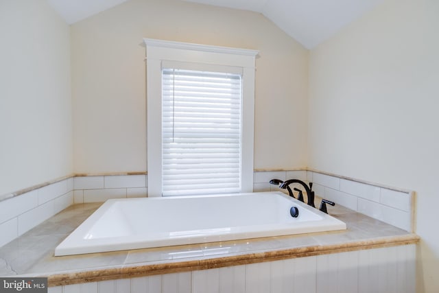 bathroom featuring tiled tub and vaulted ceiling