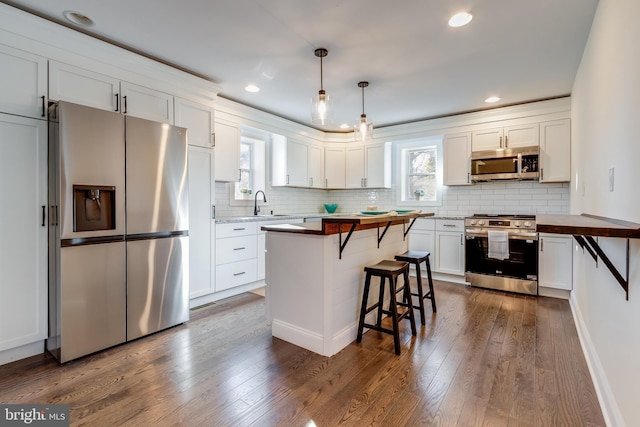 kitchen featuring white cabinets, hanging light fixtures, a wealth of natural light, appliances with stainless steel finishes, and butcher block counters