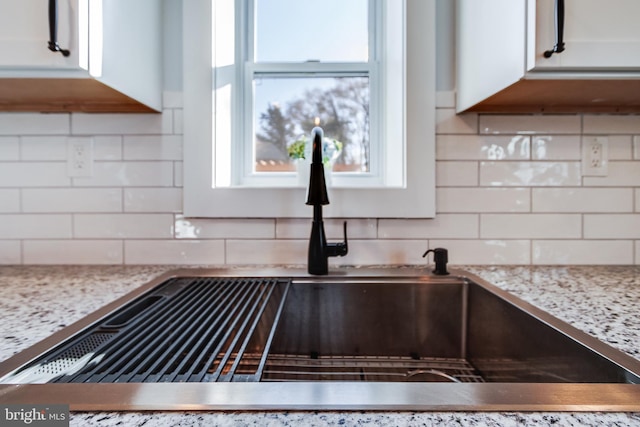 room details with tasteful backsplash, light stone countertops, sink, and white cabinets