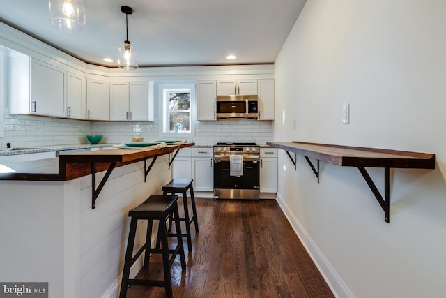 kitchen with white cabinetry, dark wood-type flooring, hanging light fixtures, stainless steel appliances, and a kitchen breakfast bar