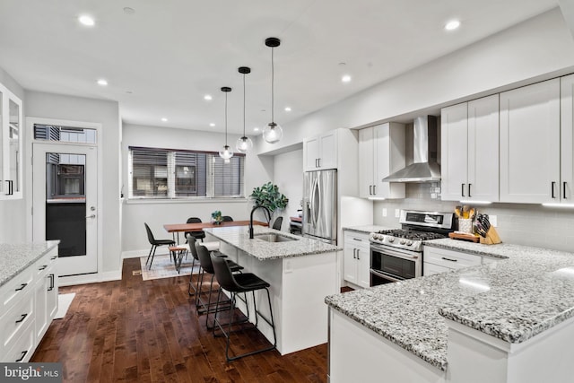 kitchen with white cabinets, a center island with sink, wall chimney exhaust hood, and appliances with stainless steel finishes