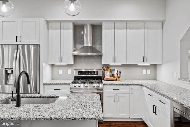 kitchen with sink, wall chimney exhaust hood, light stone counters, stainless steel fridge, and white cabinets