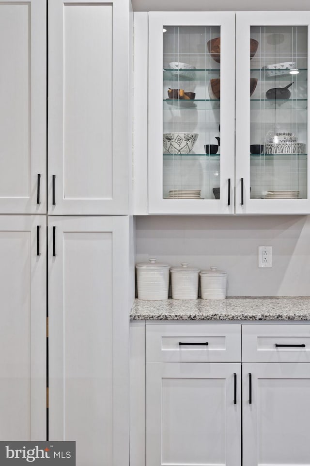 bar featuring light stone countertops and white cabinetry