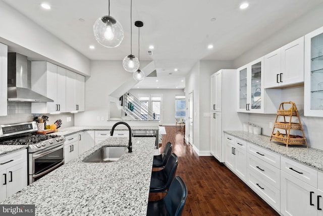 kitchen featuring white cabinets, wall chimney exhaust hood, stainless steel gas range oven, and sink