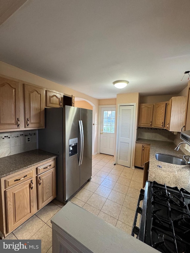 kitchen featuring stainless steel fridge with ice dispenser, black gas range, light tile patterned floors, and sink