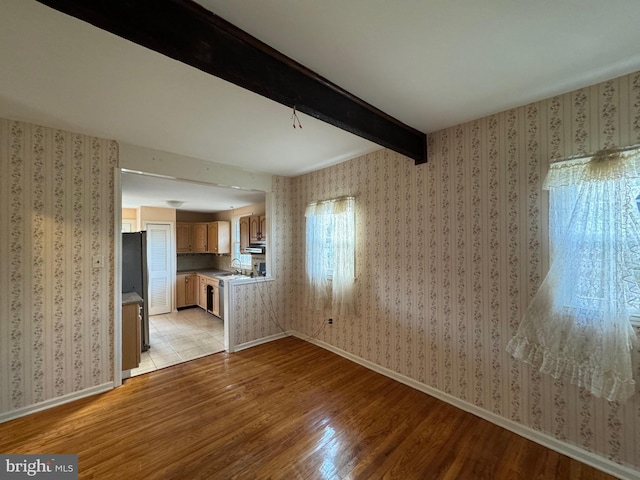 unfurnished living room with beamed ceiling, light wood-type flooring, and sink