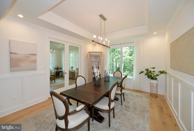 dining space with light hardwood / wood-style floors, crown molding, a raised ceiling, and a notable chandelier