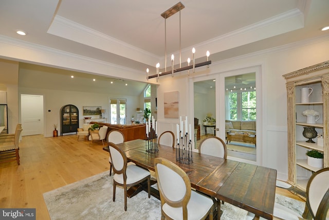 dining area featuring a raised ceiling, light wood-type flooring, ceiling fan with notable chandelier, and ornamental molding