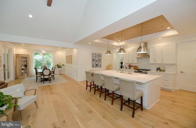 kitchen featuring white cabinets, decorative light fixtures, an island with sink, sink, and a tray ceiling