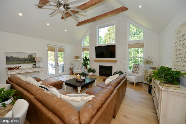 living room featuring light hardwood / wood-style floors, beam ceiling, a stone fireplace, high vaulted ceiling, and french doors