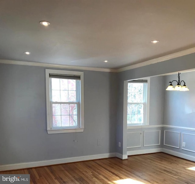 spare room with wood-type flooring, ornamental molding, and an inviting chandelier