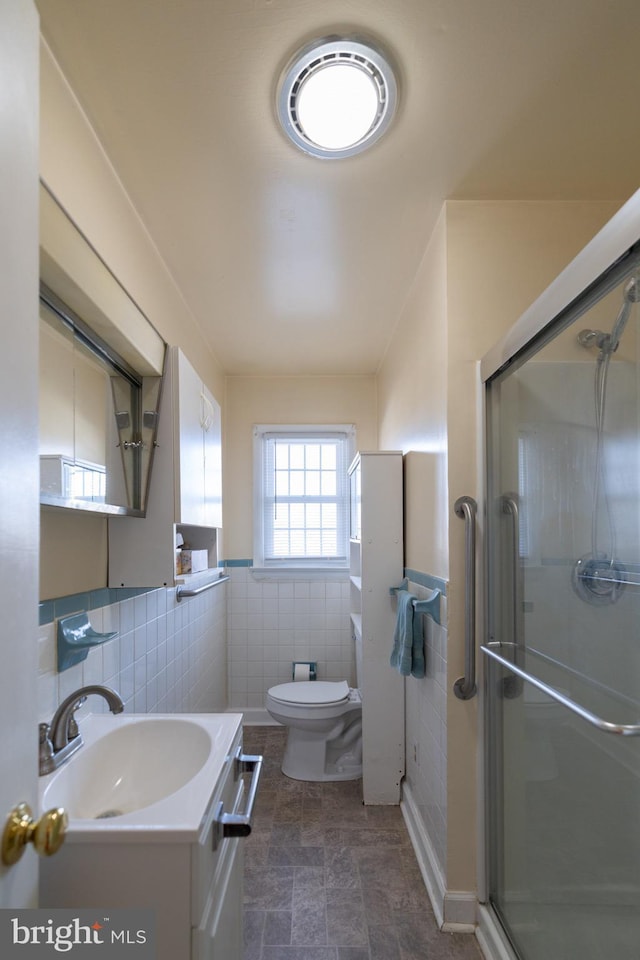 bathroom featuring vanity, toilet, a shower with door, and tile walls