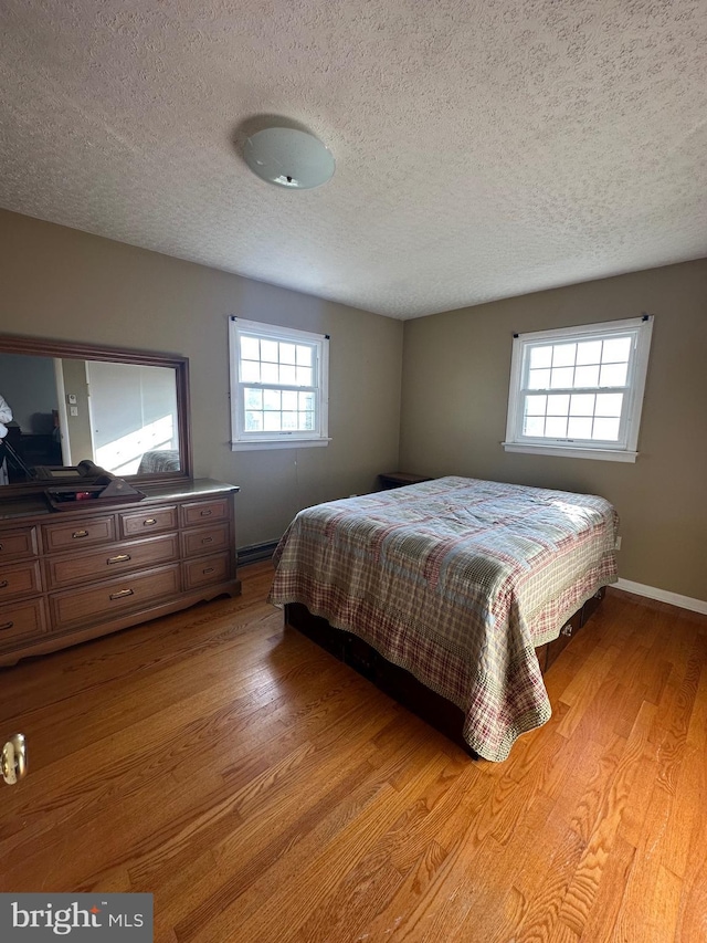 bedroom with a textured ceiling, light wood-type flooring, and multiple windows