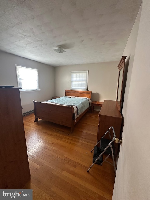 bedroom featuring a textured ceiling, light hardwood / wood-style floors, a baseboard radiator, and multiple windows