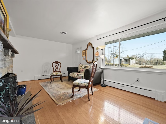 sitting room with a baseboard radiator, visible vents, a stone fireplace, and hardwood / wood-style floors