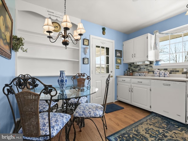 kitchen with white dishwasher, wood finished floors, white cabinets, decorative backsplash, and an inviting chandelier