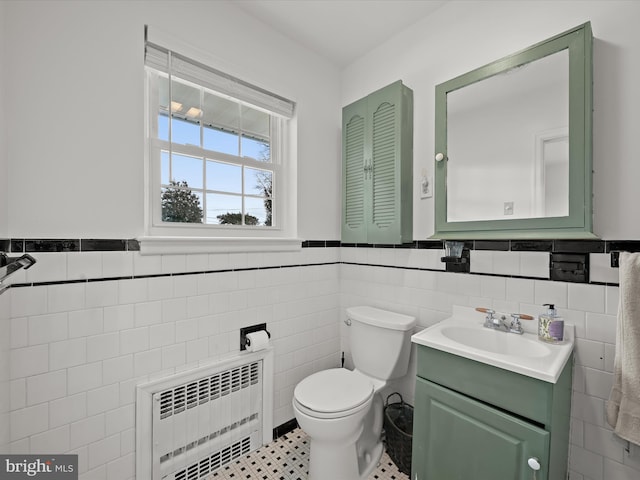 half bath with a wainscoted wall, tile walls, toilet, radiator heating unit, and vanity