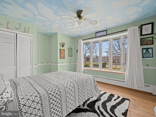 bedroom featuring a ceiling fan, a baseboard radiator, a closet, and wood finished floors