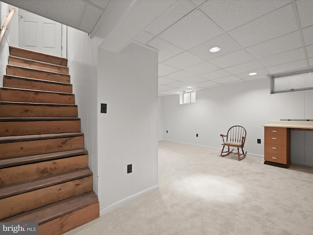 finished basement featuring stairs, a paneled ceiling, and light colored carpet