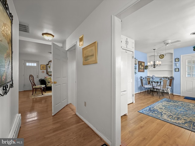 hallway with visible vents, baseboards, wood finished floors, a baseboard heating unit, and a notable chandelier