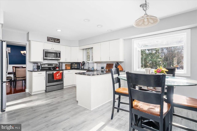 kitchen with decorative backsplash, light wood-type flooring, stainless steel appliances, white cabinets, and hanging light fixtures