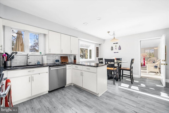 kitchen with kitchen peninsula, stainless steel dishwasher, sink, pendant lighting, and white cabinets