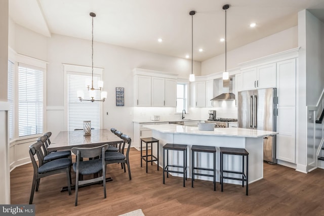 kitchen featuring white cabinets, wall chimney range hood, hanging light fixtures, and dark wood-type flooring