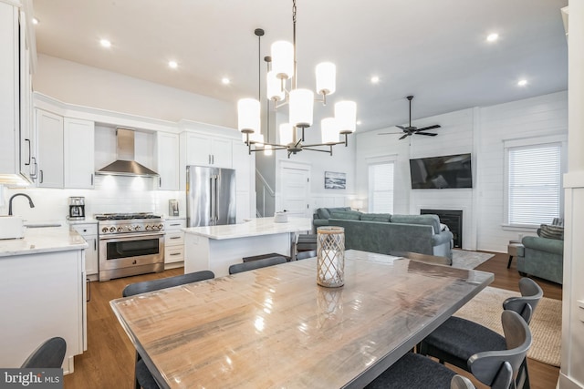 dining space featuring dark wood-type flooring, ceiling fan with notable chandelier, sink, a fireplace, and a wealth of natural light