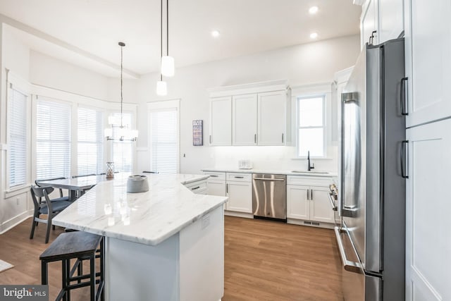 kitchen with hardwood / wood-style flooring, appliances with stainless steel finishes, decorative light fixtures, a kitchen island, and white cabinetry