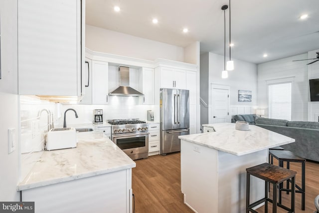 kitchen with wall chimney exhaust hood, high end appliances, sink, white cabinets, and a center island